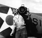 Photographer's Mate Robert F. Read, standing with an aerial camera in front of a Scouting Six plane.